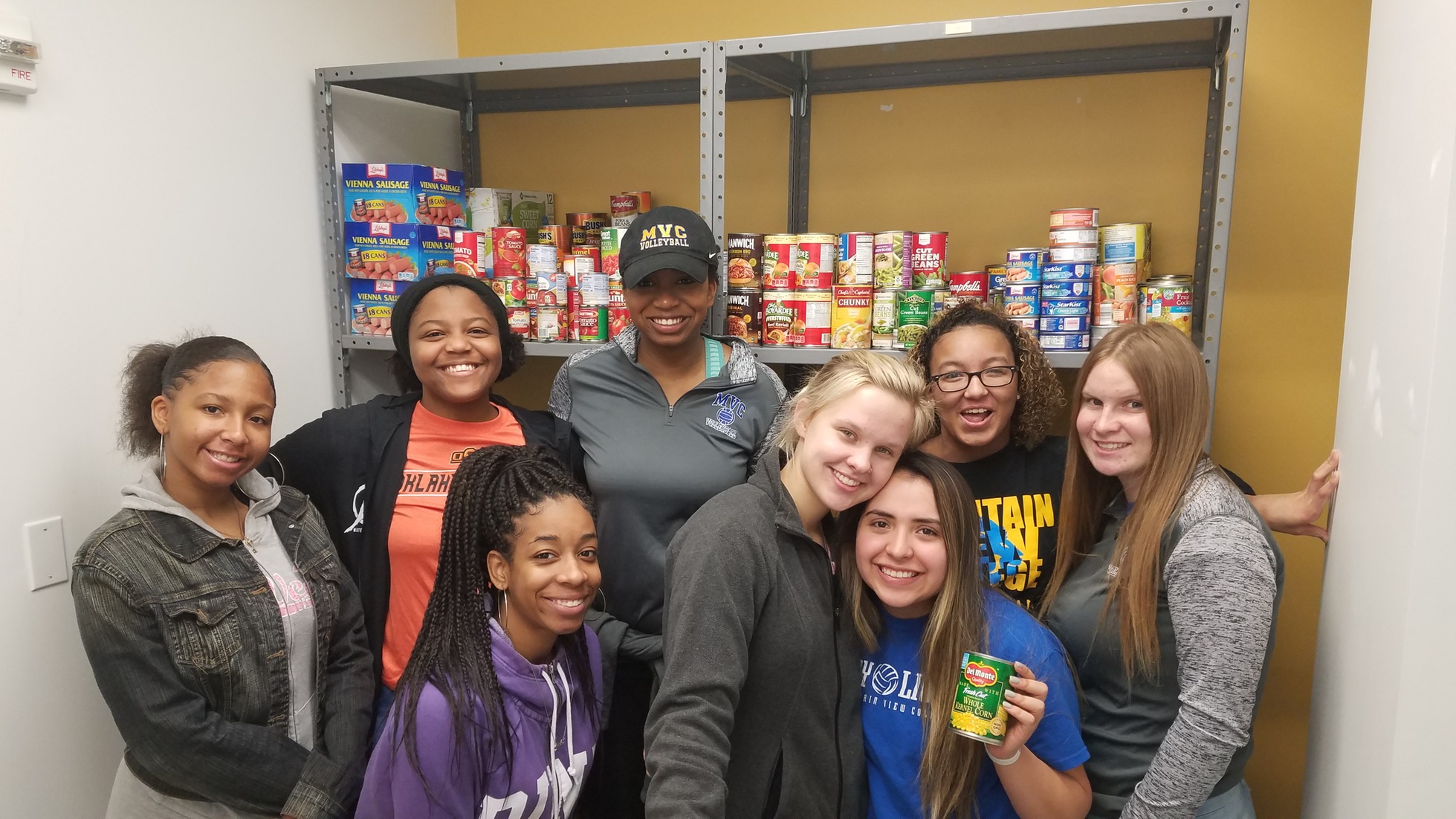Volleyball team poses in front of canned goods.